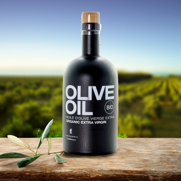 Black Olive Oil bottle sat on a table in front of a olive field