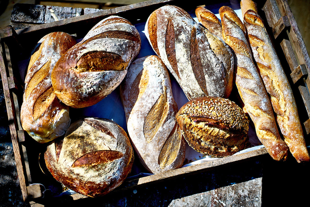 A wooden crate containing a selection of freshly baked bread covered in flour and seeds